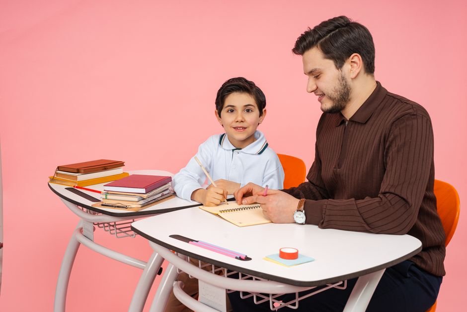 A school-age child writing at a desk while a parent helps